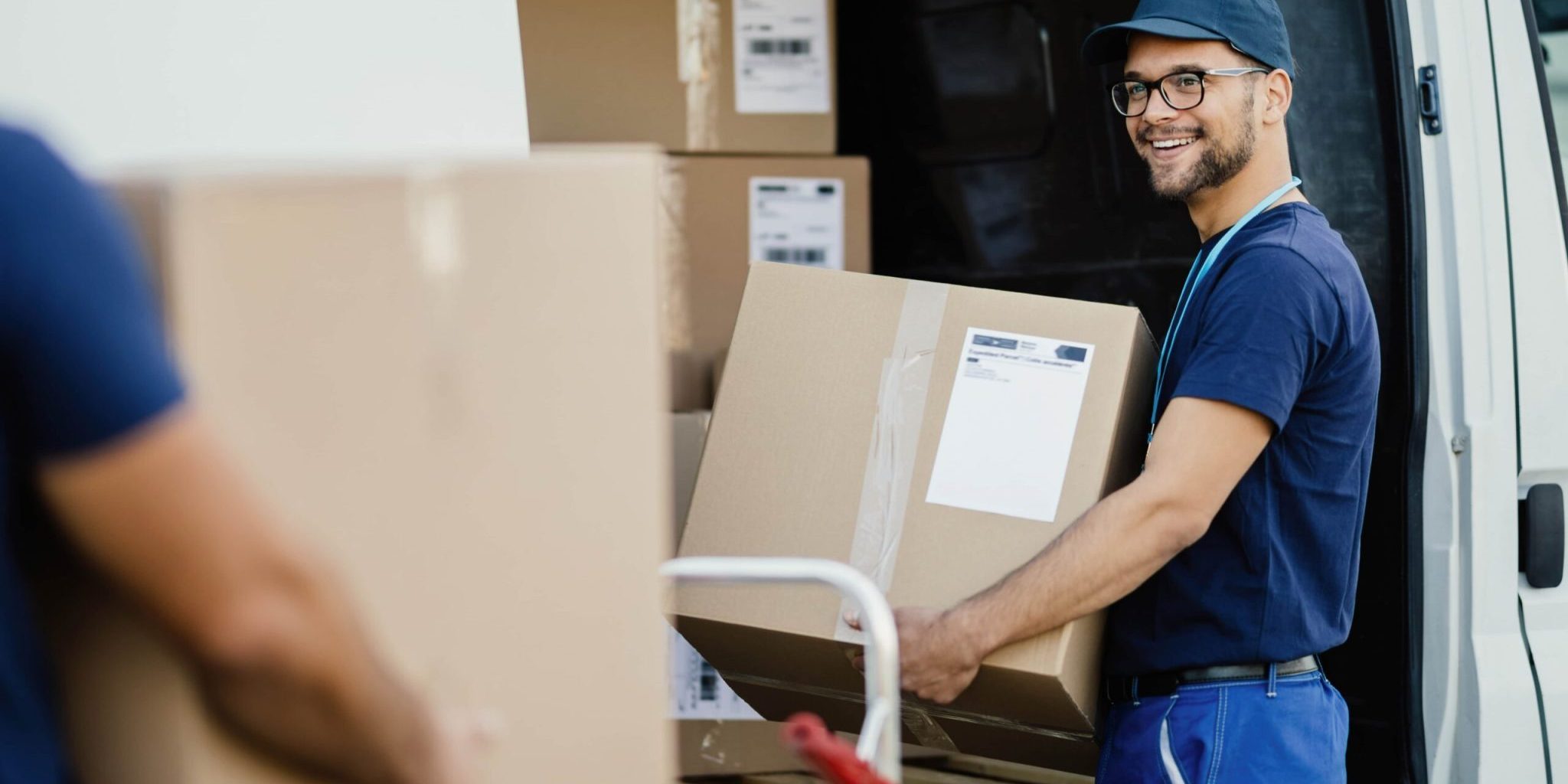 young-happy-manual-worker-carrying-cardboard-boxes-delivery-van-while-communicating-with-his-colleagues-min bezorging