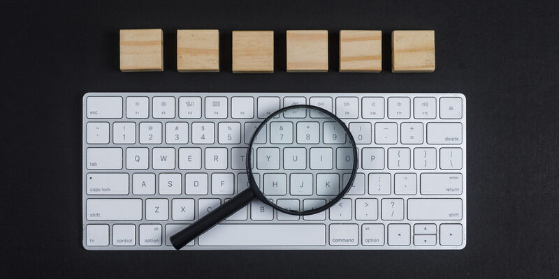 Conceptual of research with keyboard, magnifier, wooden cubes on black desk background flat lay. horizontal image Vergrootglas op toetsenbord als symbool voor SEO content analyse en Google beoordeling.